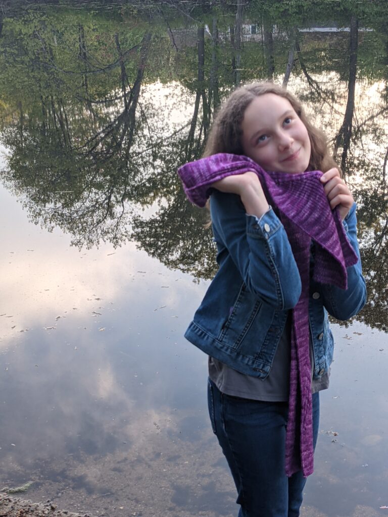 Girl rubs the Nicondo Scarf on her cheek in front of a reflective pond