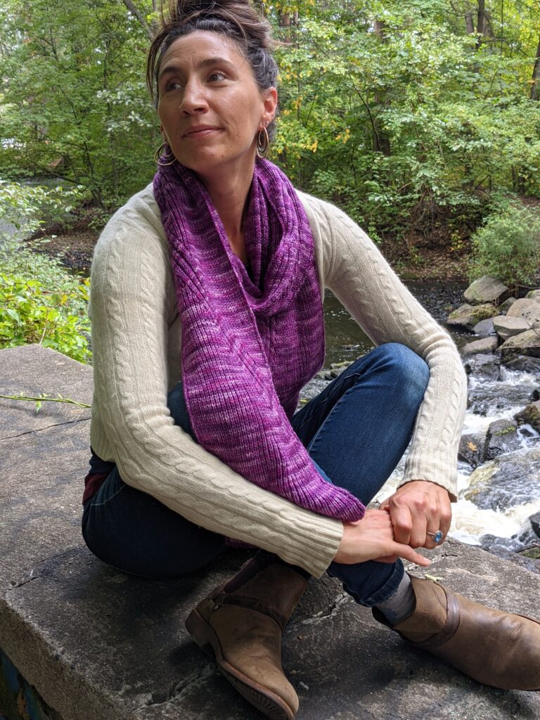 Woman sits cross legged on a wall overlooking a waterfall wearing the Nicondo Scarf