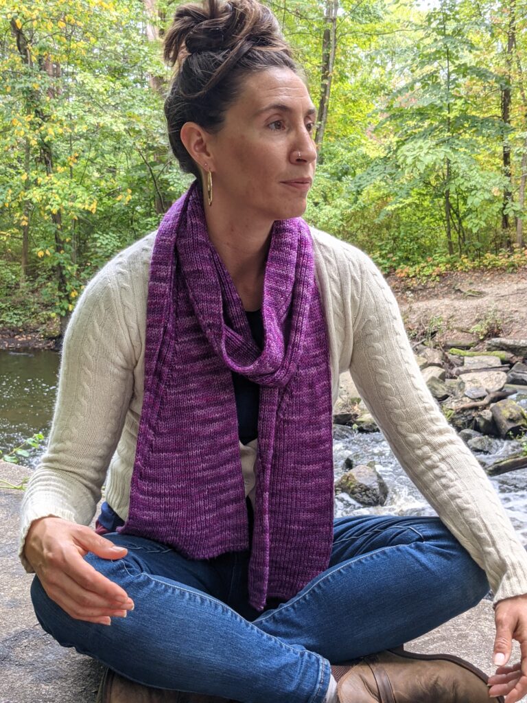 Woman wearing the Nicondo scarf sits cross legged gazing to the right