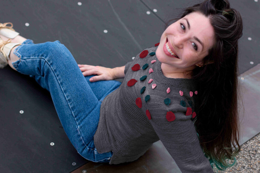 Smiling woman looks at the camera over her shoulder in digitally altered grey Circle Dance Sweater