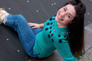 Woman smiles over her shoulder wearing a fitted Circle Dance Sweater digitally altered to appear to be the pale green colorway from Space Cadet Yarns