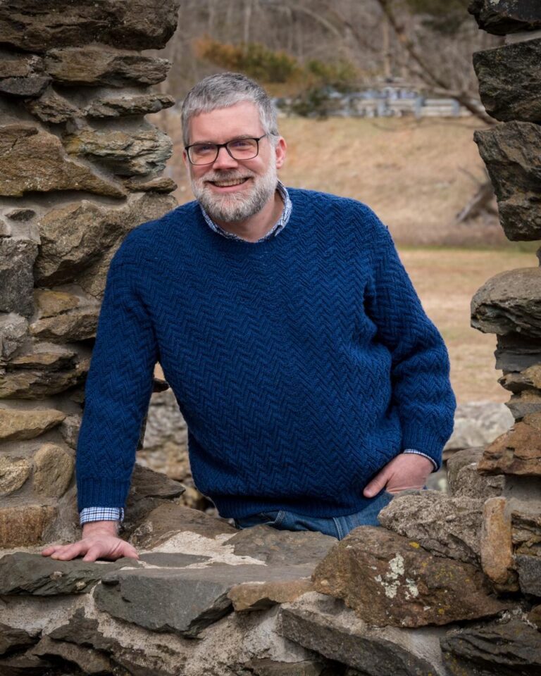 Man wearing Herring Run Sweater seen through the window of colonial ruins