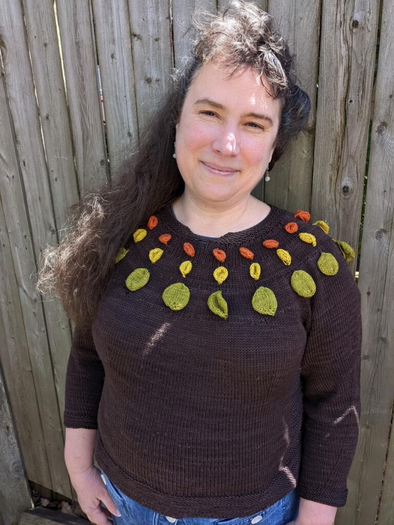 Christine Guest wearing the prototype for Circle Dance Sweater in front of a weathered fence