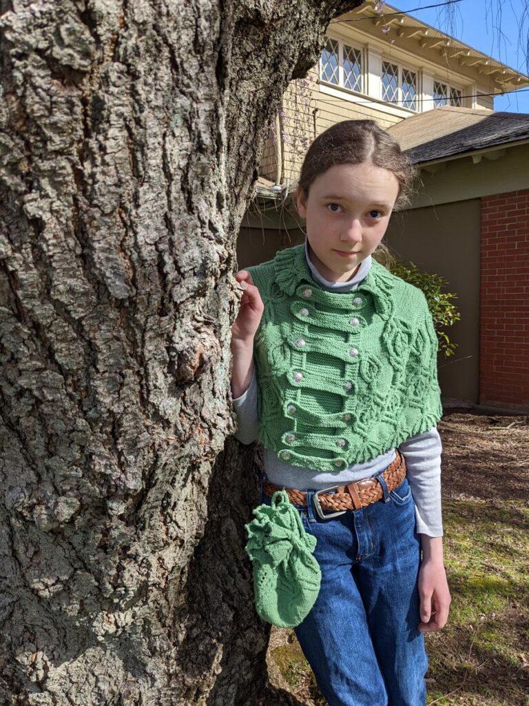 Girl leans against a tree wearing the Silvia of ELF cape and the Silvia Needs a Bag bag.