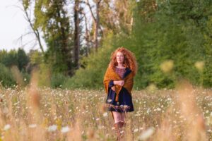 Front View of Hollywood and Vine shawl, worn over a blue dress in meadow.Photo by Elizabeth Zimmerman of Western Rose Studios.